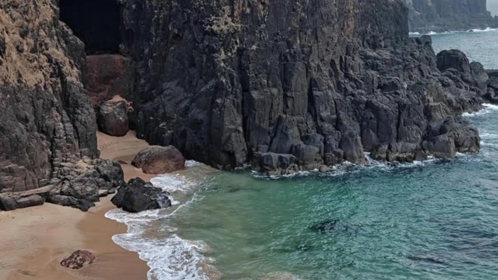 Black rock cliffs above a turquoise hidden Kokan cove