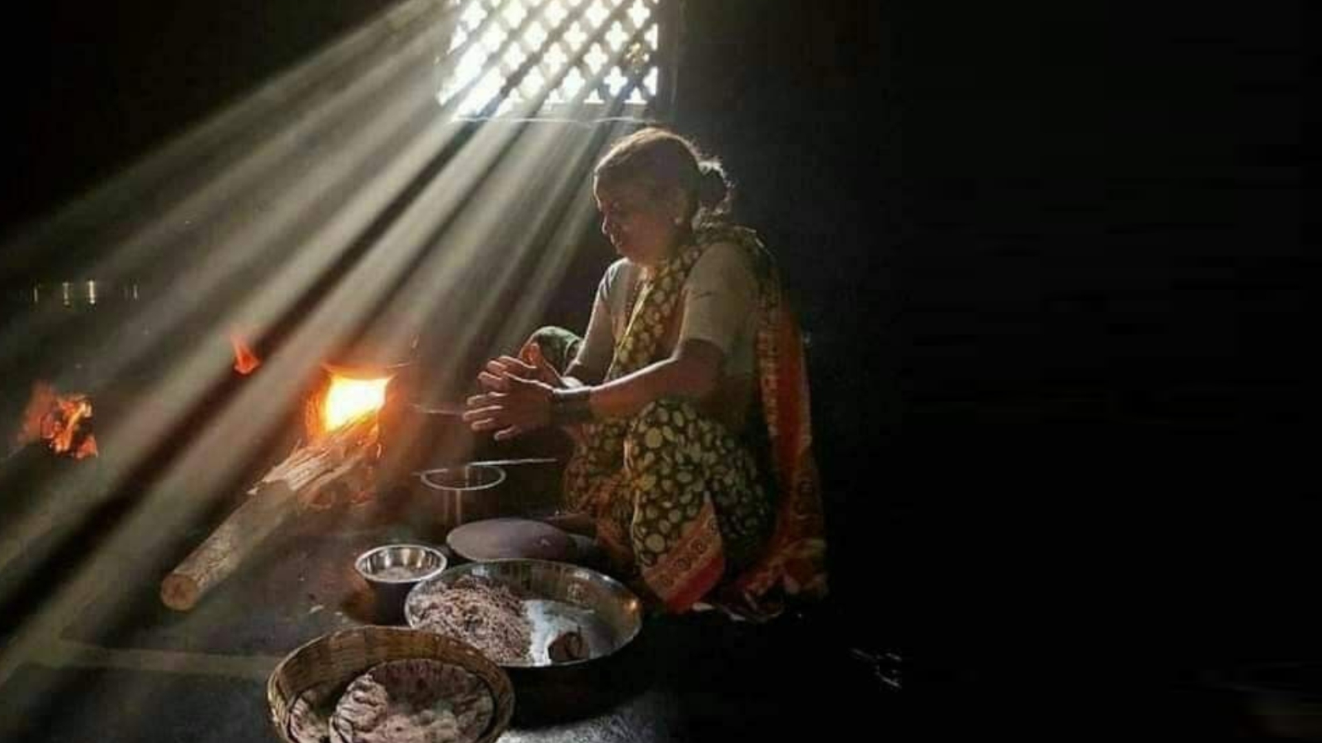 Woman cooking on a traditional wood chulha in soft morning light