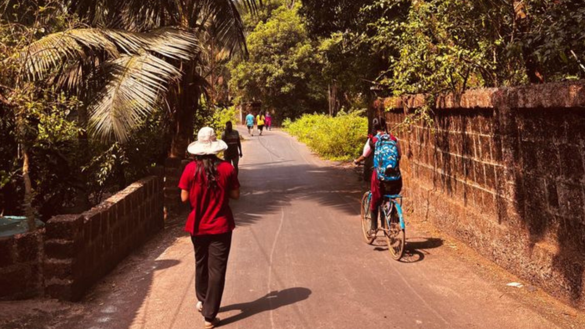 Cyclists and walkers on a quiet laterite-walled village road