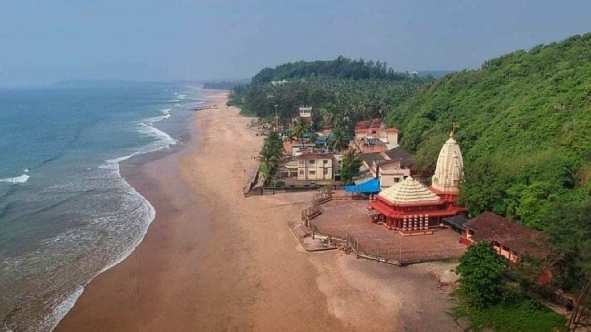 Aerial view of a sweeping beach with a seaside temple and village
